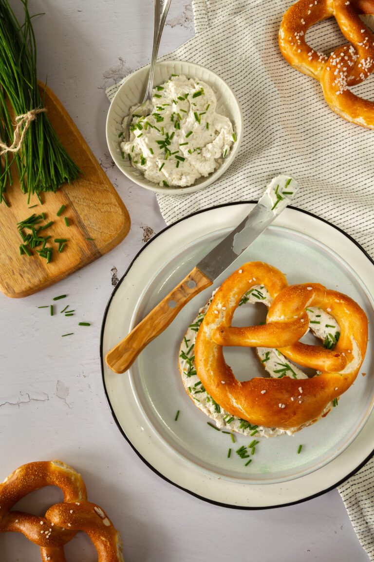 Frische Breze mit veganem Frischkäseaufstrich und Schnittlauch serviert.