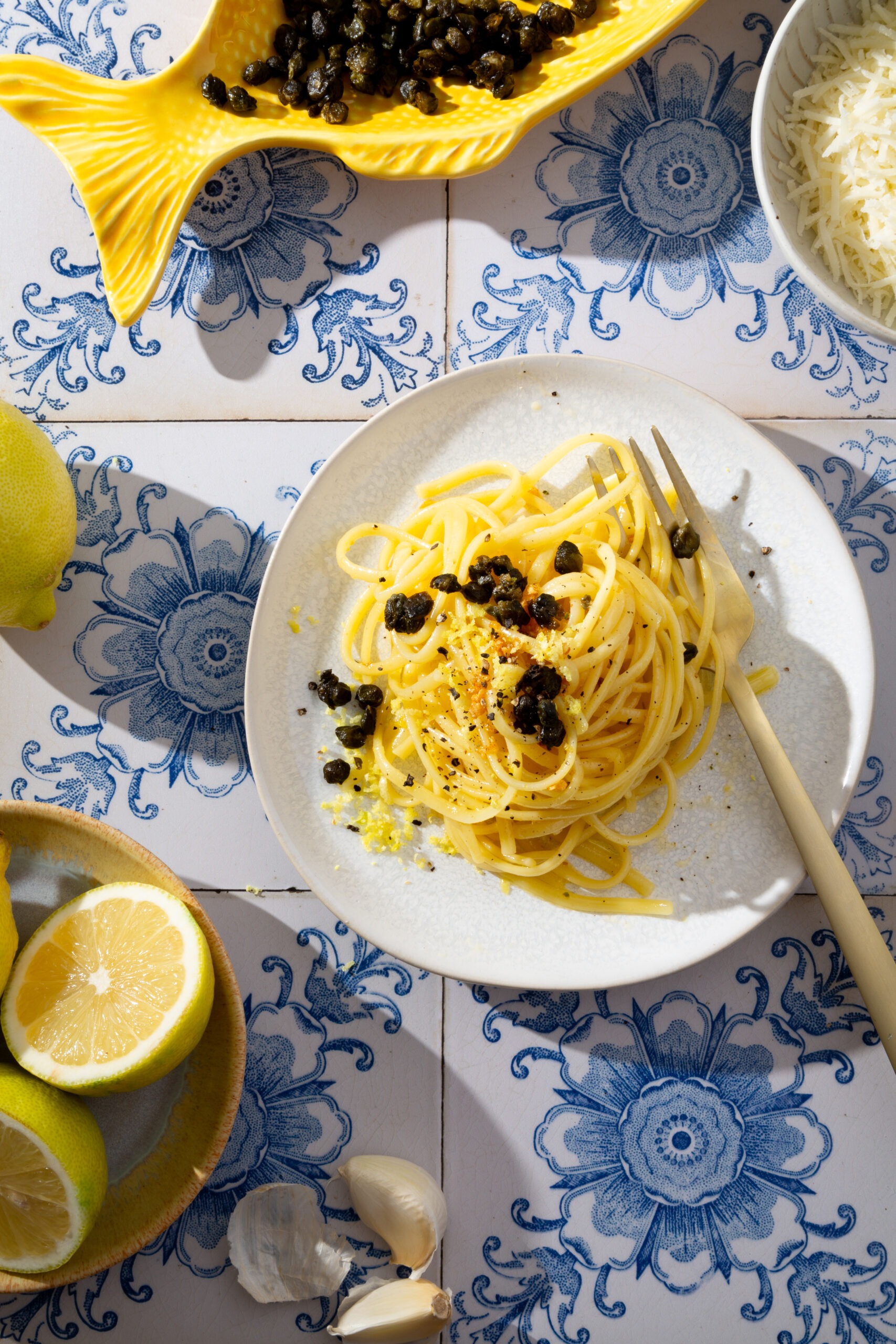 Zitronen-Butter Pasta mit frittierten Kapern auf einem mediterranen Fliesen Untergrund.