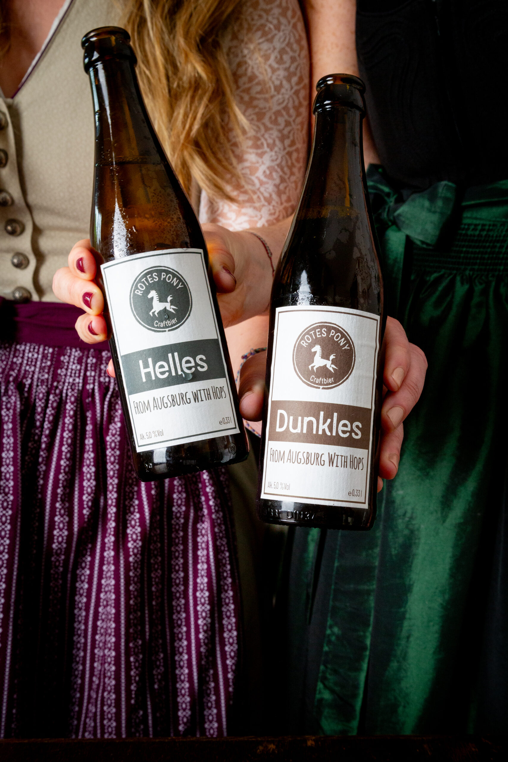 Rotes Pony Helles und Dunkles Bier gehalten von zwei Frauen mit Dirndl.